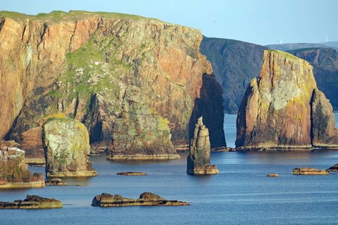 Coastal landscape with majestic cliffs in the sunlight by the blue sea, Dore Holm, Hillswick,
