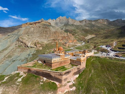 Old fortress embedded in dramatic mountain scene with cloudy sky and rocky heights, aerial view,