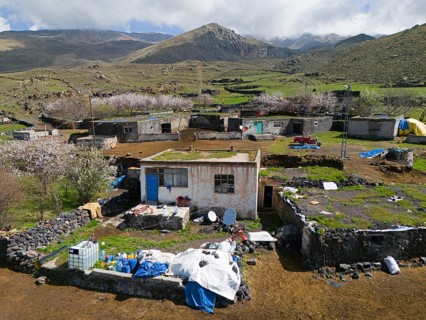 Rural village with simple houses and lots of greenery in mountainous terrain under a cloudy sky,
