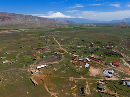 Expansive landscape with a village and a snow-capped mountain on the horizon under a blue sky,