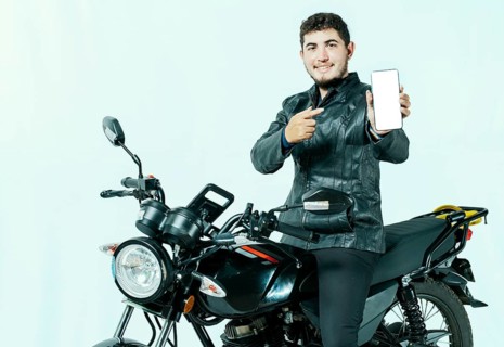 Young motorcyclist sitting on his motorcycle showing cell phone screen isolated. Male biker on his