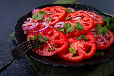 Freshly sliced tomatoes and red onions, garnished with herbs, on a black plate, summer salad, no