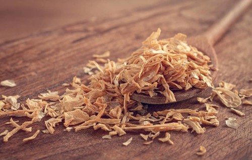 Smoked onion flakes, on a wooden spoon, wooden table, close-up