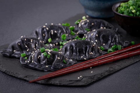 Japanese gyoza dumplings, made of black dough, black gyoza, with green onions and sauce, on a