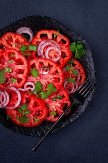 Freshly sliced tomatoes and red onions, garnished with herbs, on a black plate, summer salad, no
