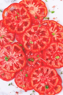 Freshly sliced ripe tomatoes arranged on a marble surface with microgreens and sea salt for a