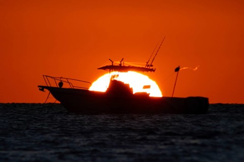 The sun rises behind a boat on the Costa Rei, a coastal stretch of the Italian Mediterranean island