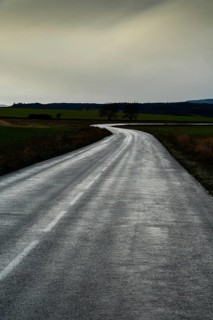 A winding road stretches through green fields under a cloudy sky, showcasing the beauty of the