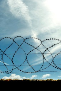 A barbed wire fence stretches across the foreground, silhouetted against a clear blue sky with