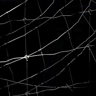 Worn netting stretches across a dark backdrop, showcasing intricate patterns and textures. The play