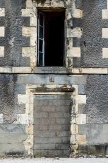 An abandoned structure stands with a weathered gray facade and an open window, highlighting urban