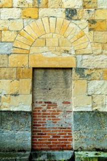 An old stone wall showcases a prominently arched doorway, leading to an unseen area beyond. The