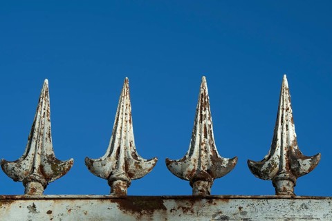 Four rusted metal spikes rise prominently against a vivid blue sky, showcasing weathered details