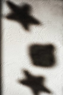 Shapes of stars and a square cast shadows on a textured white wall, illuminated by gentle light.