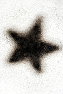 A dark star-shaped shadow is visible on a light-textured wall, creating a striking contrast that