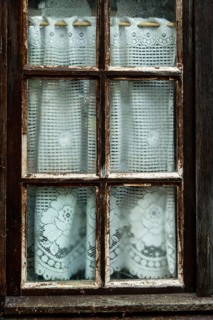 The rustic window displays delicate lace curtains with intricate floral designs, slightly dampened