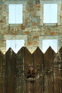 A weathered wooden fence stands in the foreground, with a charming stone house featuring white