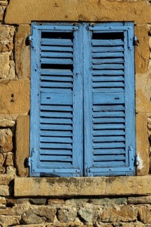 Bright blue shutters adorn the weathered stone wall of a traditional building in a picturesque