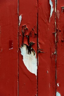 A close-up view captures the peeling red paint on a wooden surface, showcasing intriguing textures