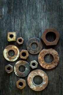 Various rusty nuts are scattered across an old wooden surface, revealing their distinct shapes and