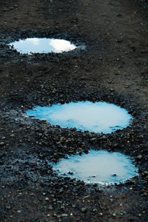 Three puddles on a gravel path mirror the overcast sky, highlighting the damp texture of the ground