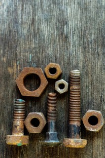 Various sizes and shapes of rusty bolts and nuts are displayed on a weathered wooden surface. Soft