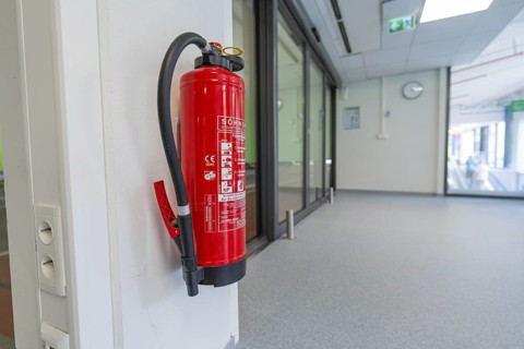Red fire extinguisher on a white wall in the office corridor, Care Connect, vaccination kiosk for