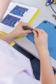 Person studying a circuit board and a manual on a table with a blue background