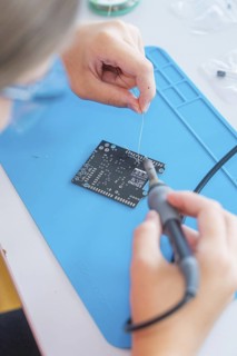Person uses a soldering iron to work on a printed circuit board on a blue base