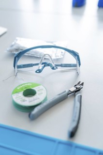 Safety goggles, pliers and solder on a table for electronics work