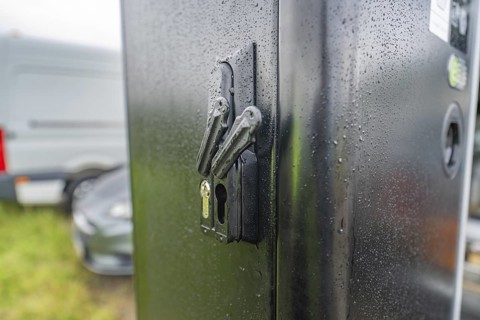 Security lock on a rain-soaked, black housing next to a parked car, installation of a charging