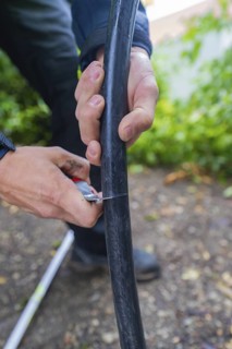 Hands cutting a black cable outdoors with a small cutting tool, assembly of a charging station for
