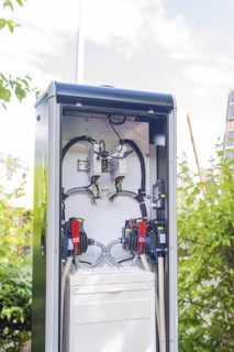 An open outdoor power box in front of a blue sky and green bushes, installation of a charging