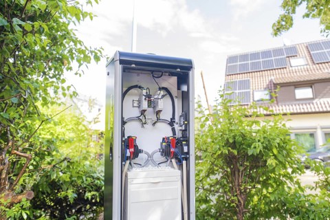 A power box in the garden with solar panels on the house in the background, installation of a