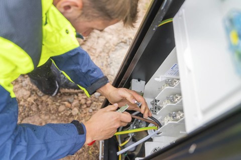 A person uses a tool to carry out work on an electrical switch box, assembly of a charging station