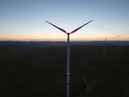 A wind turbine in front of a colourful evening sky with the silhouette in the darkness,