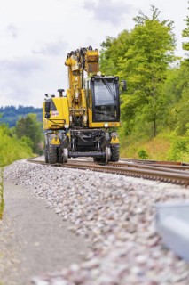 Large yellow machine runs on rails, surrounded by trees and clouds, grinding work on the Hermann