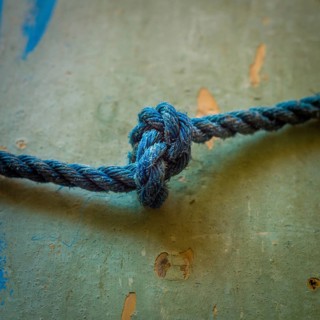 A close-up view reveals an intricately tied blue rope knot resting on a textured surface,