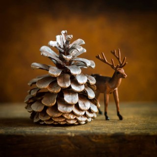 A charming deer figurine stands next to a large pine cone, evoking a cozy winter ambiance. This