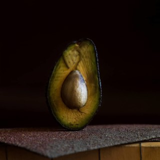 A half avocado is placed on a rough, textured surface, highlighting its smooth, creamy interior and