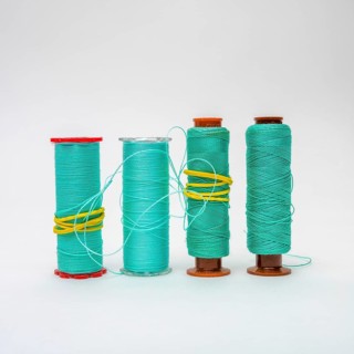 A collection of turquoise bobbins of thread is displayed, showcasing different sizes and textures