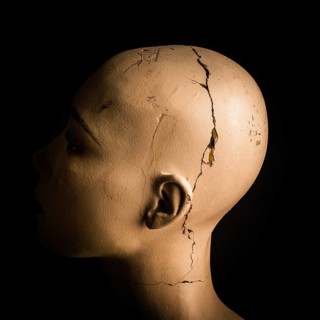 A head of a broken woman dummy is positioned in profile. The damaged surface reveals cracks and