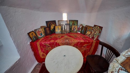 A table with red blankets and several icons flanked by candles in a small room, chapel, church,