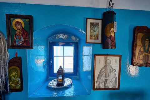 Blue painted wall with various religious pictures around a small window, chapel, church, Agios