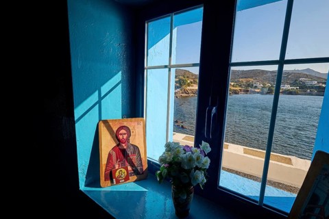Icon on a windowsill overlooking the sea, surrounded by blue light and a bouquet of flowers,