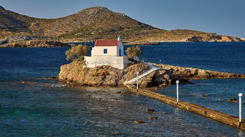 Whitewashed chapel on island, accessible via footbridge, surrounded by calm blue water, chapel,