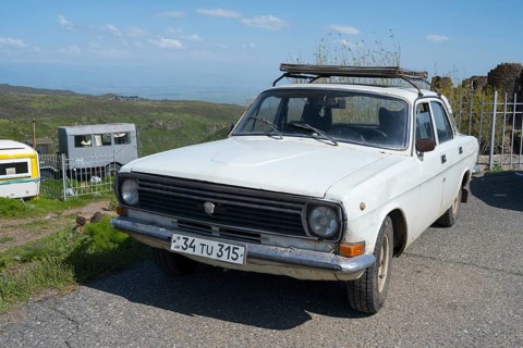 An old car is standing on a rural road with mountains and clear sky in the background, vintage car,