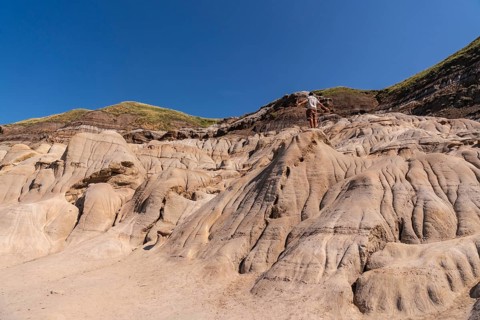 Tourist standing on a hoodoo rock formation, exploring the unique badlands landscape of drumheller,
