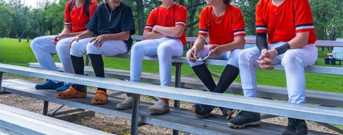 Young baseball players sitting together on bleachers, enjoying camaraderie and conversation after a