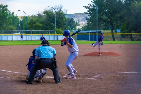 Teenage baseball batter waiting for the pitch while the pitcher is throwing the ball during a sunny